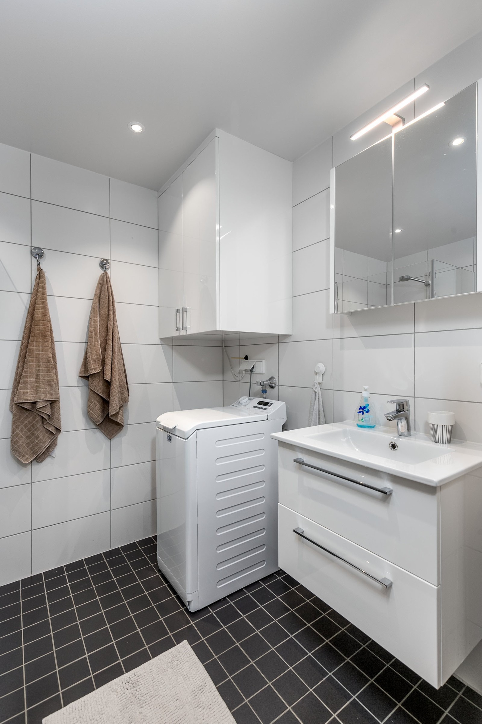 Smakfullt bad med flislagte overflater og varmekabler i gulv. Innredningen består av moderne servantmøblement i hvit høyglans med 2 skuffer, speilskap, tilhørende veggskap og toalett.